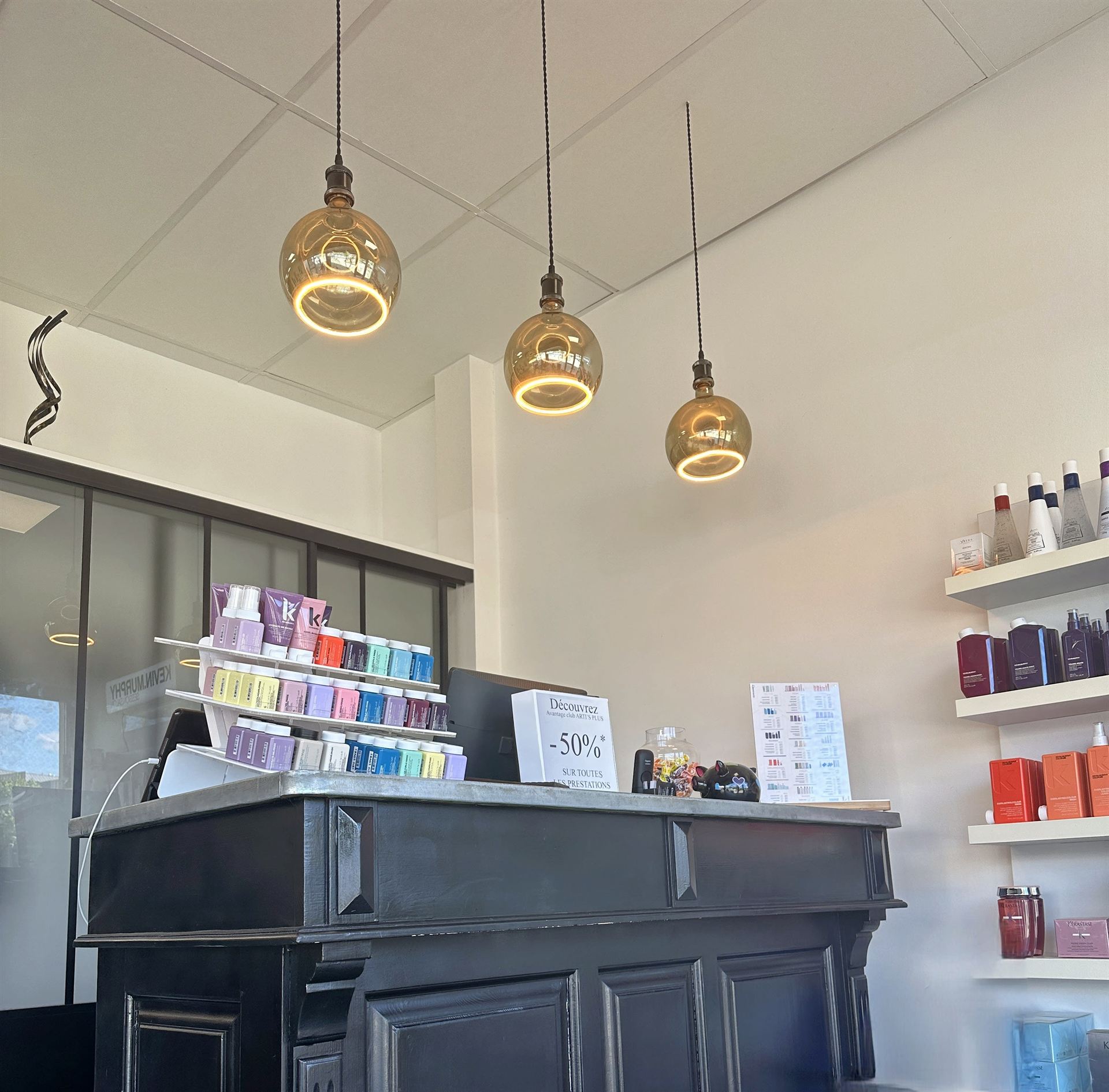 Comptoir d'accueil noir et suspensions dorées du salon Arti's Coiffure
